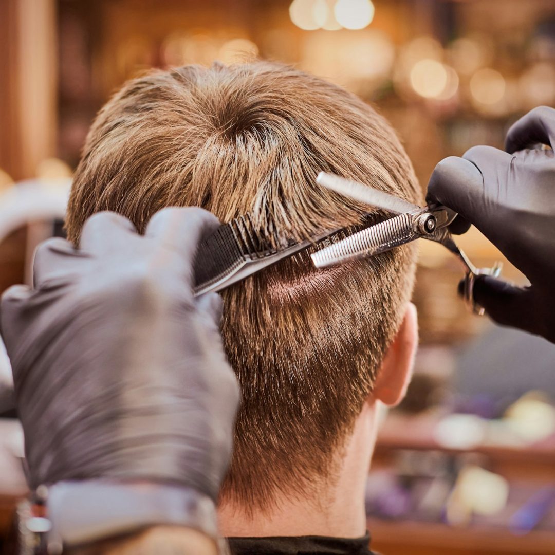 Male haircut in barbershop close up, client getting haircut by hairdresser with comb and scissors