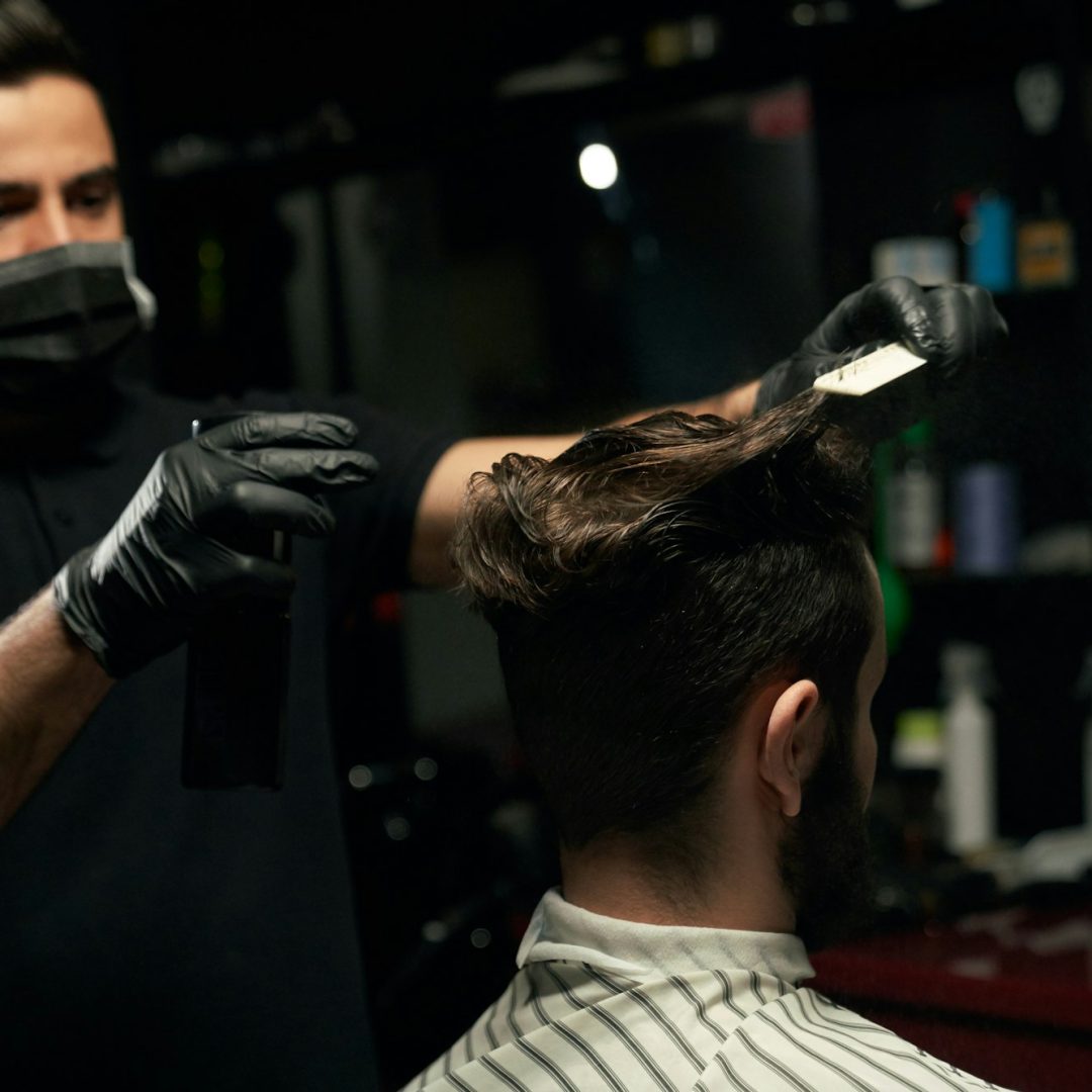 Male professional barber doing hair styling to handsome guy